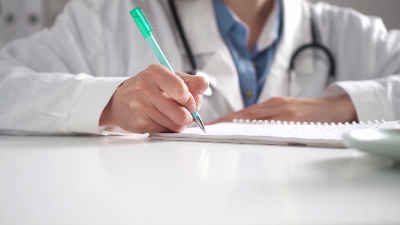 一位女医生坐在她的办公桌前，用钢笔填写医疗文件视频下载