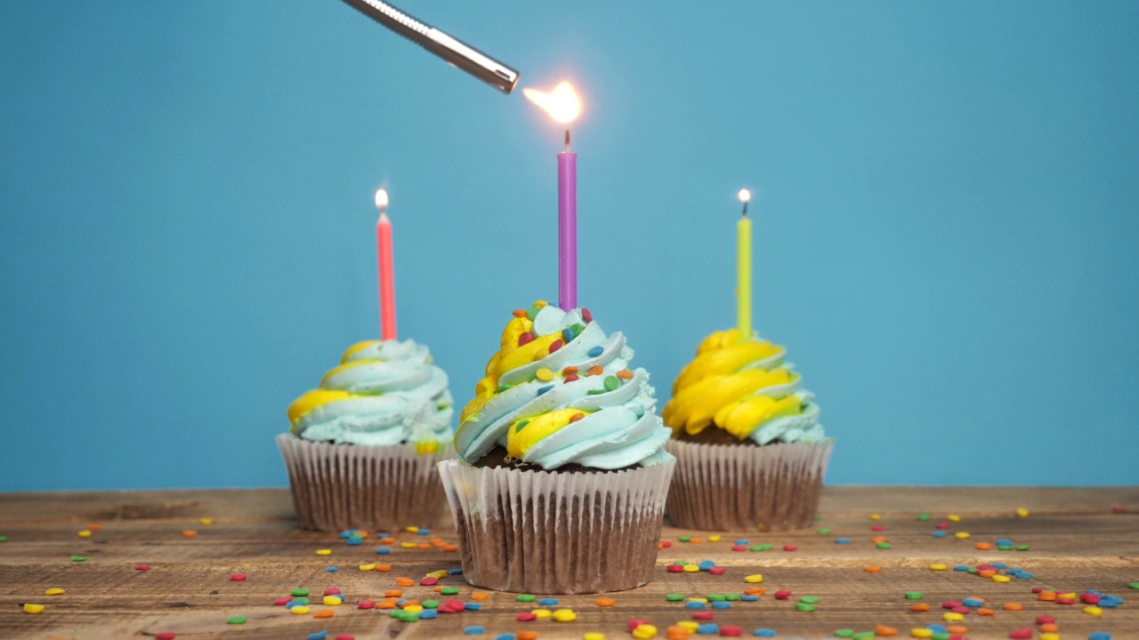 生日纸杯蛋糕，蓝色背景上有蜡烛和装饰品。生日快乐的问候。在纸杯蛋糕上点一支蜡烛视频素材