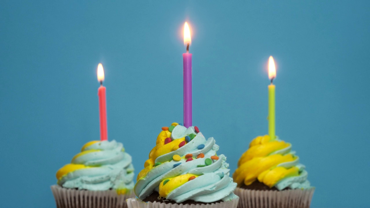 生日纸杯蛋糕，蓝色背景上有蜡烛和装饰品。生日快乐的问候。在纸杯蛋糕上点一支蜡烛视频素材