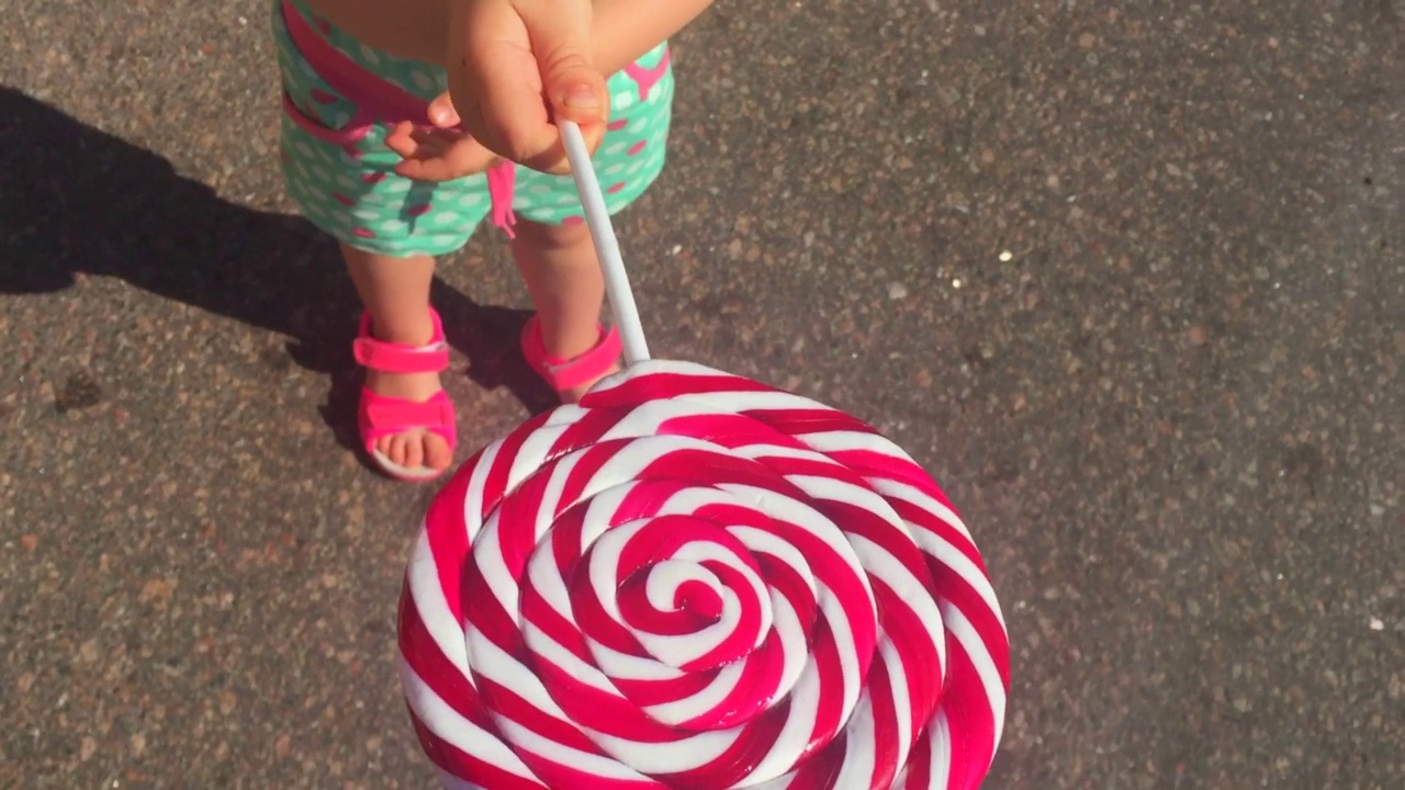 4岁的白人小女孩吃着又大又圆的棒棒糖。视频素材