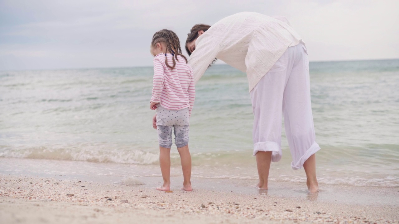 母亲和小女儿在海边散步海滩上幸福的一家人母亲牵着孩子的手在海边散步。暑假旅行视频素材