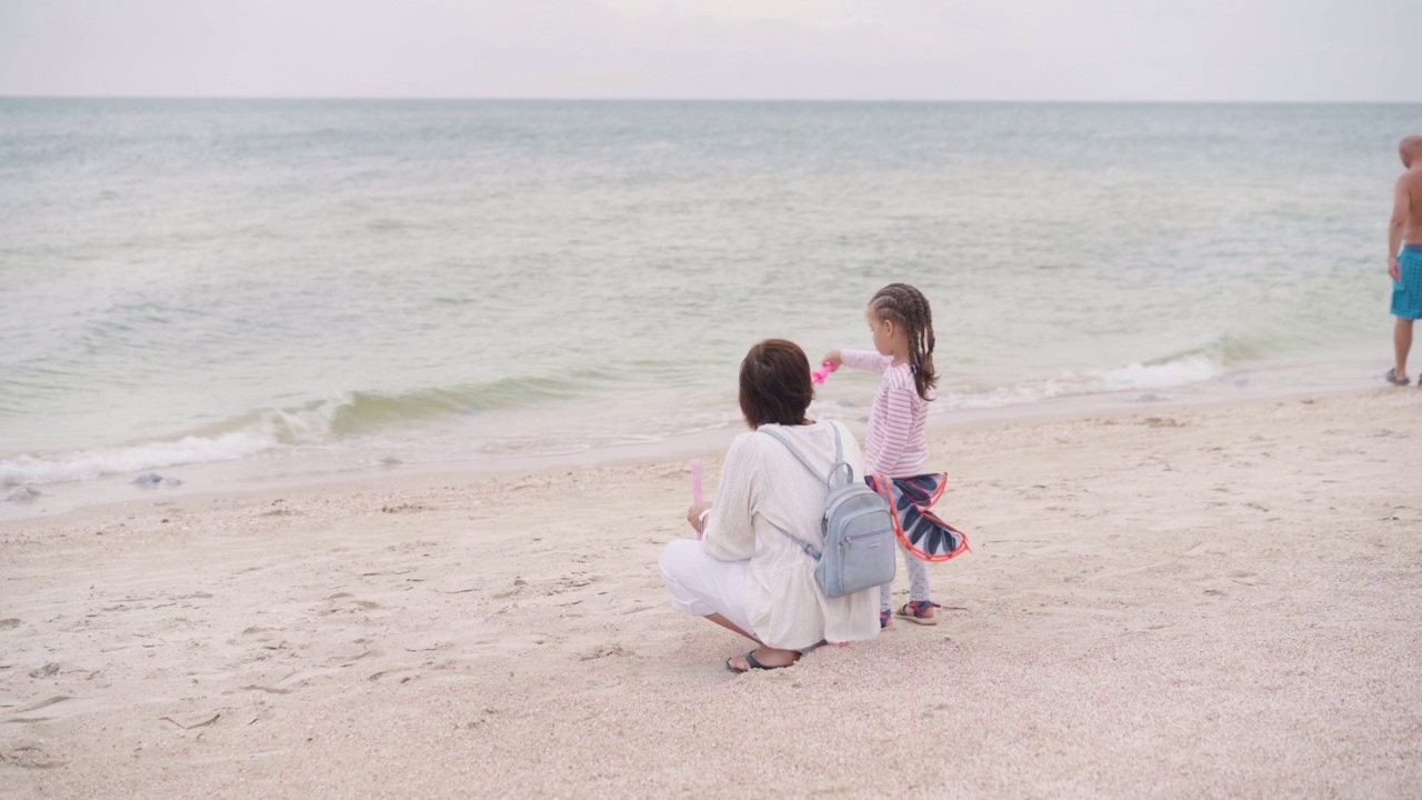 母亲带着孩子吹着肥皂泡在海滩上与一个孩子的家庭旅行暑假视频素材