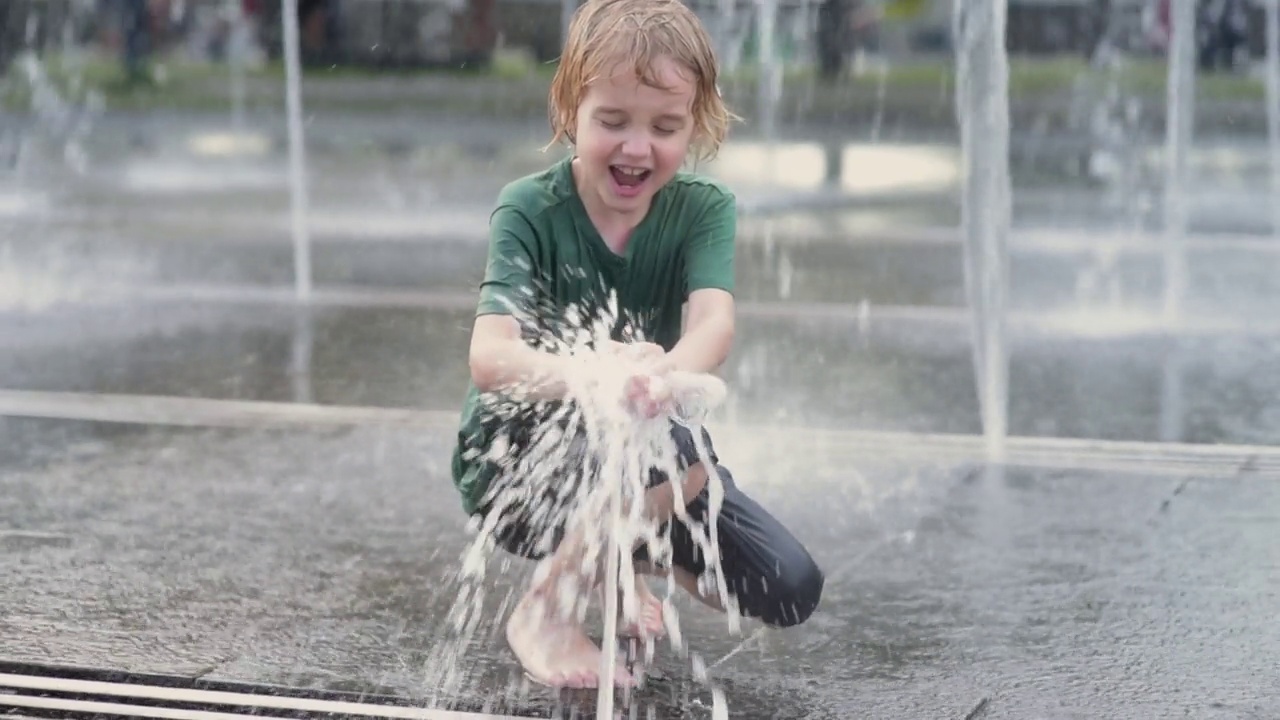 一个阳光明媚的夏日，小男孩在城市喷泉的喷泉之间的广场上玩耍。城市孩子们活跃的夏季休闲活动。视频素材