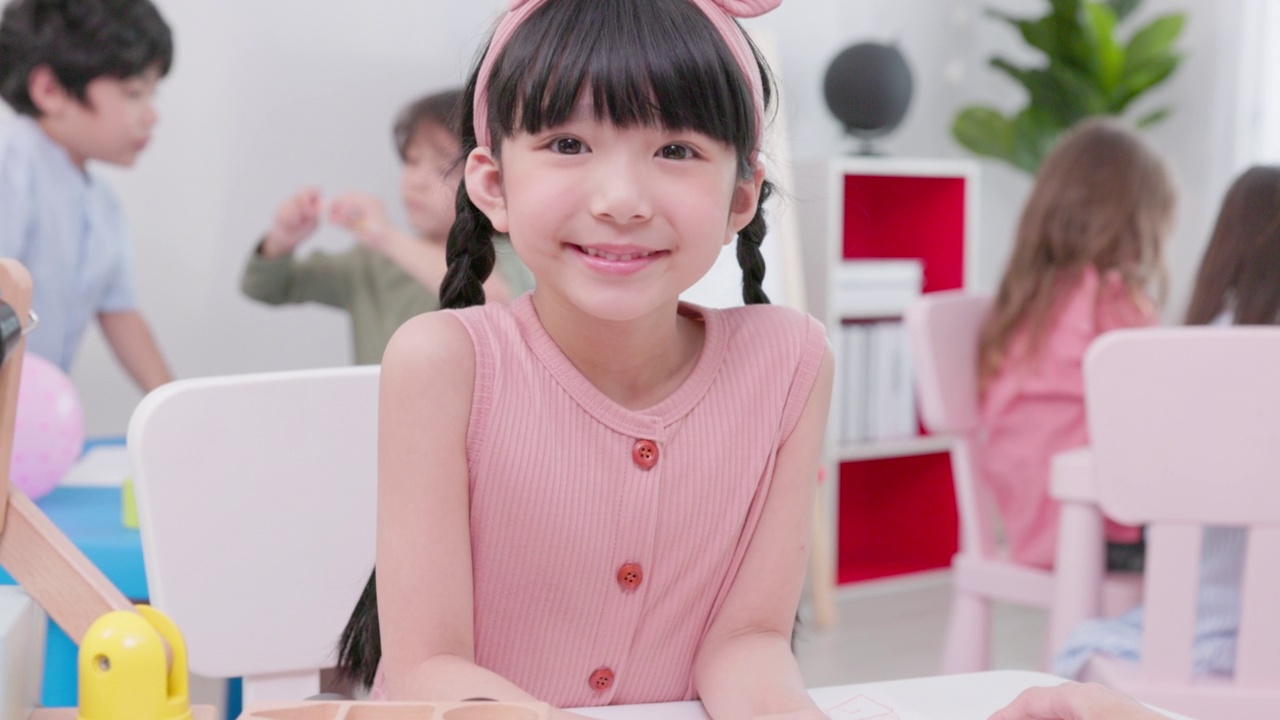 一个可爱的女孩的微笑肖像勤奋工作在幼儿园的教室与不同的聪明的孩子们视频下载