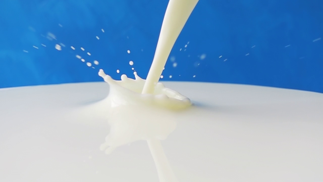牛奶倒在牛奶表面的特写与美丽的飞溅和滴在蓝色的背景。4k原始慢动作视频60帧/秒。用高速电影摄影机拍摄，1000帧/秒。视频素材