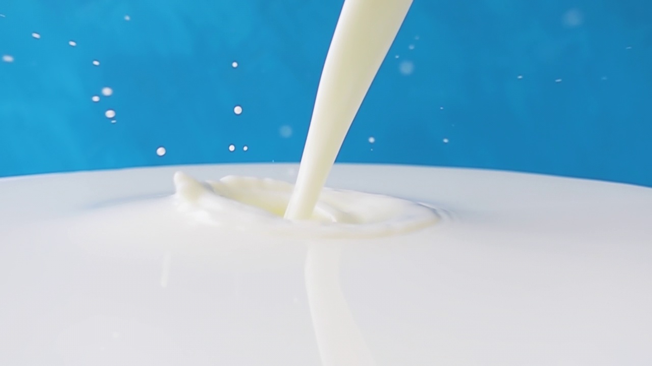 牛奶倒在牛奶表面的特写与美丽的飞溅和滴在蓝色的背景。4k原始慢动作视频60帧/秒。用高速电影摄影机拍摄，1000帧/秒。视频素材