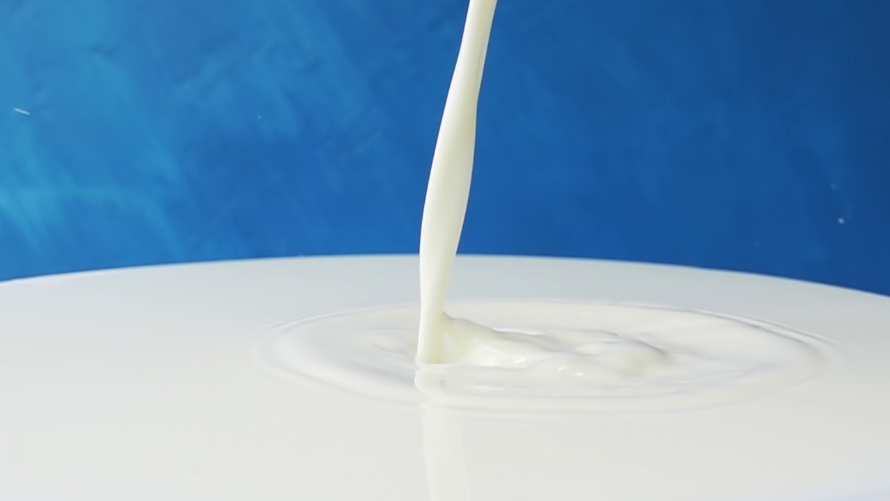 牛奶倒在牛奶的表面特写与美丽的飞溅和滴在蓝色的背景。4k原始慢动作视频60帧/秒。用高速电影摄影机拍摄，每秒1000帧。视频素材