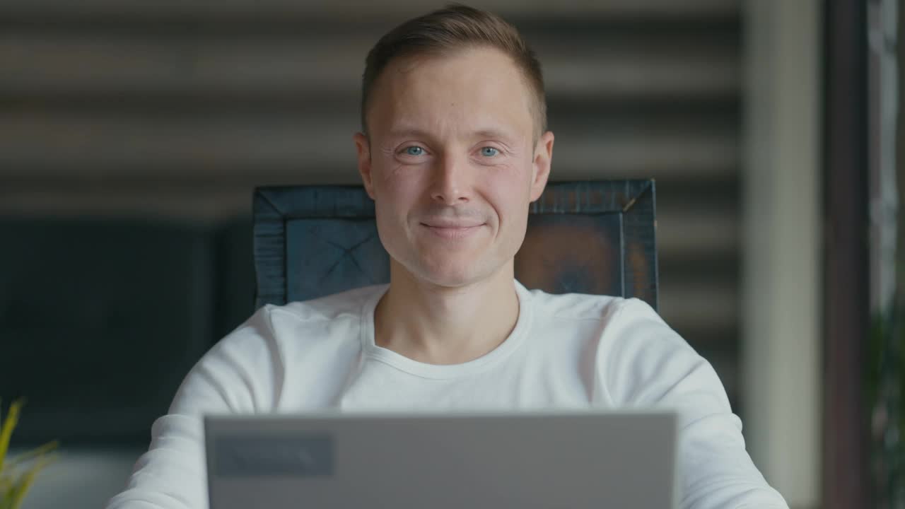 微笑的年轻人坐在房间里的笔记本电脑前的肖像视频素材