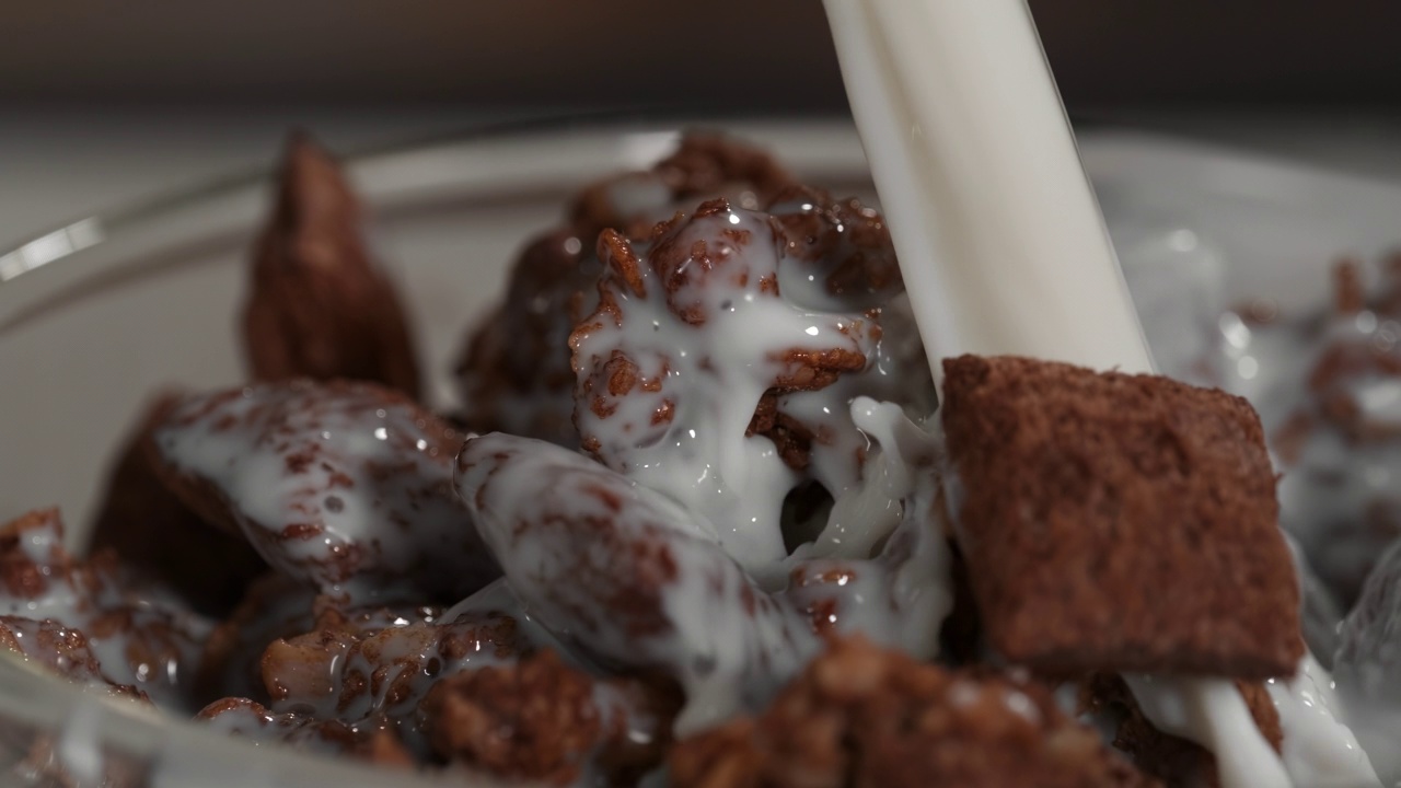 用慢动作将牛奶倒入一碗脆脆的巧克力什锦奶昔中。视频素材
