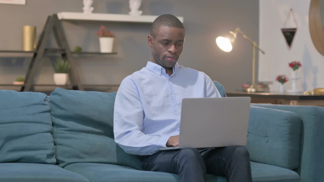 拿着笔记本电脑的非洲人在沙发上咳嗽视频素材