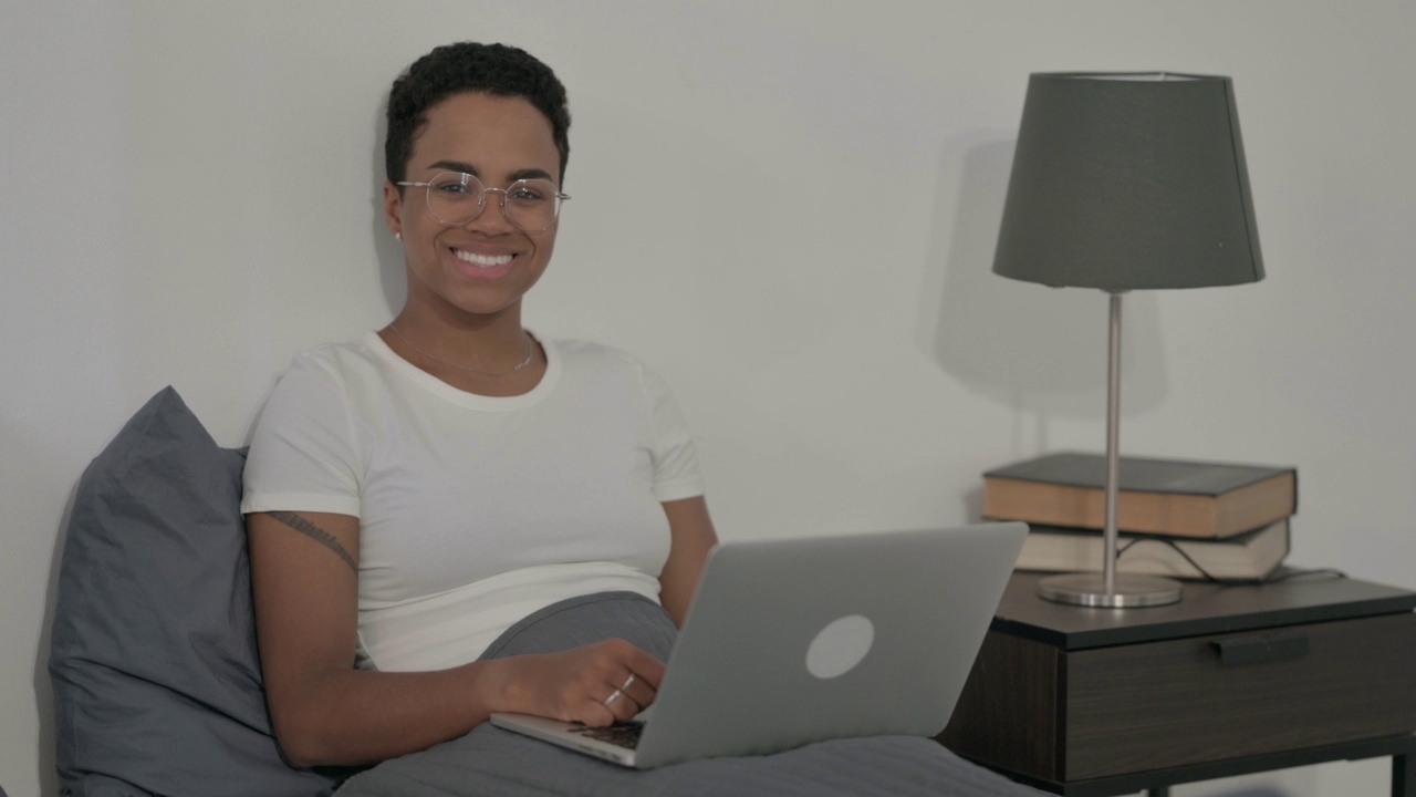 非洲妇女在床上使用笔记本电脑时对着相机微笑视频素材