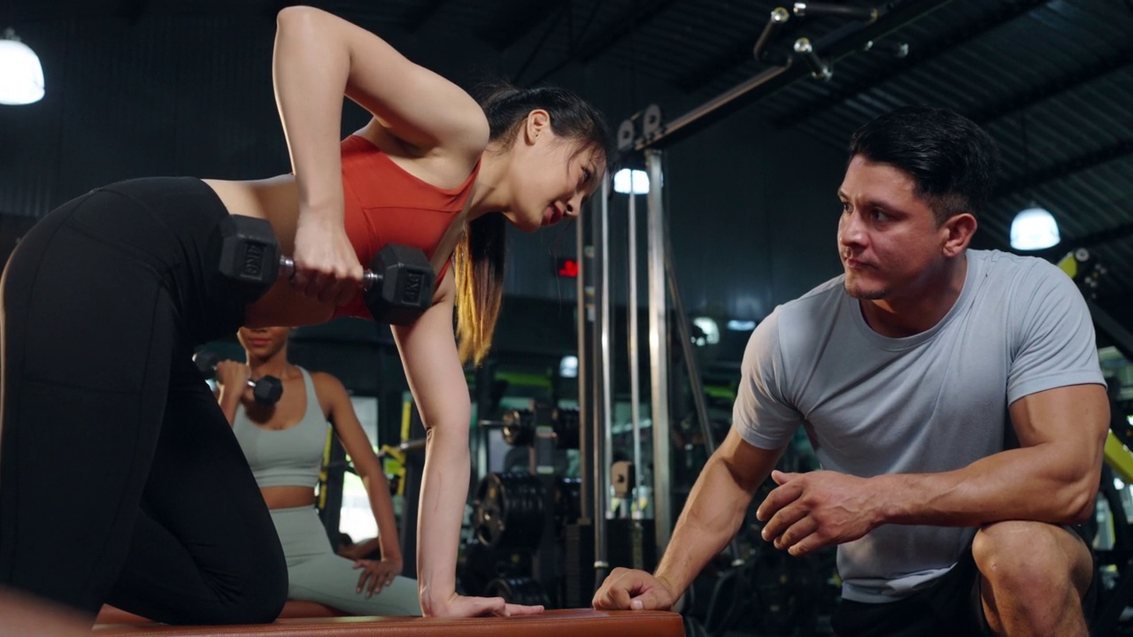 4K亚洲女子做重量训练锻炼举重哑铃与男性运动教练在健身房。视频下载