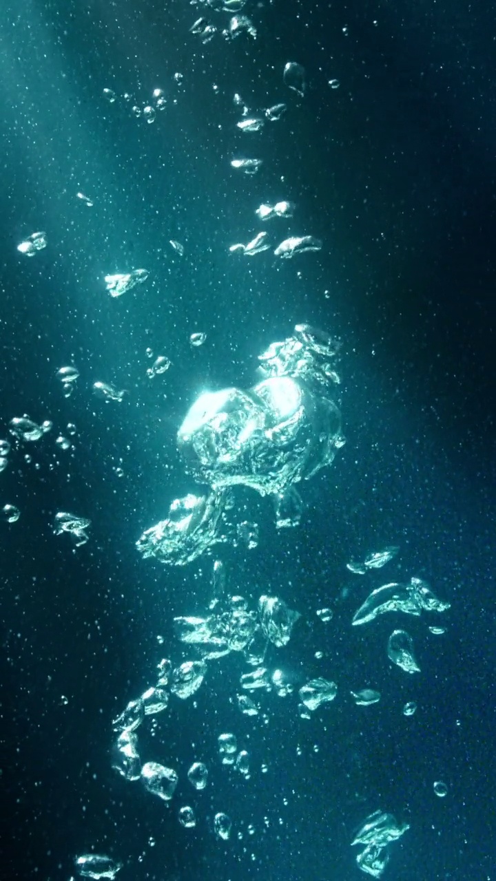近距离和超慢运动的各种大小的气泡从底部在深海与阳光从顶部照耀下的气泡在深绿色的背景视频购买