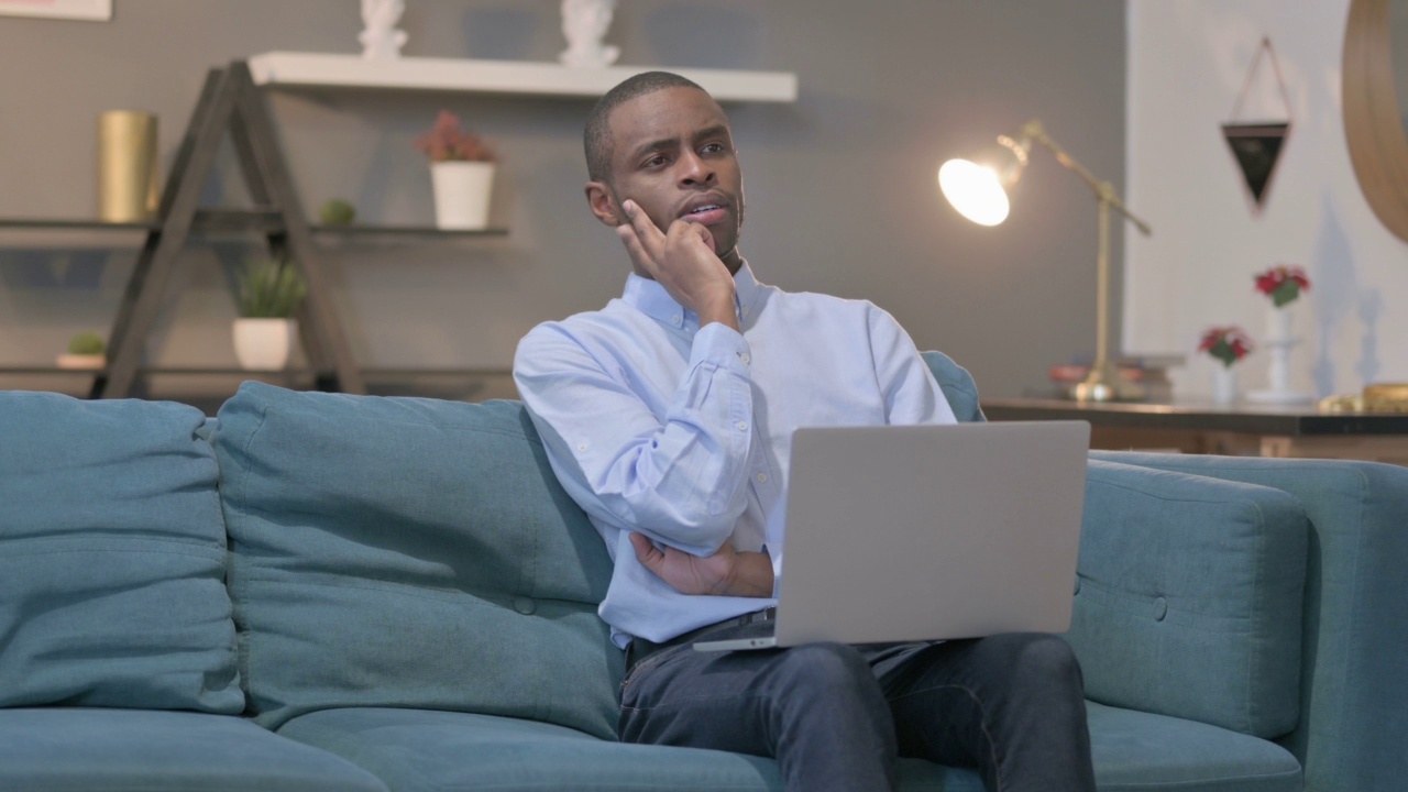 非洲人拿着笔记本电脑在沙发上思考视频素材