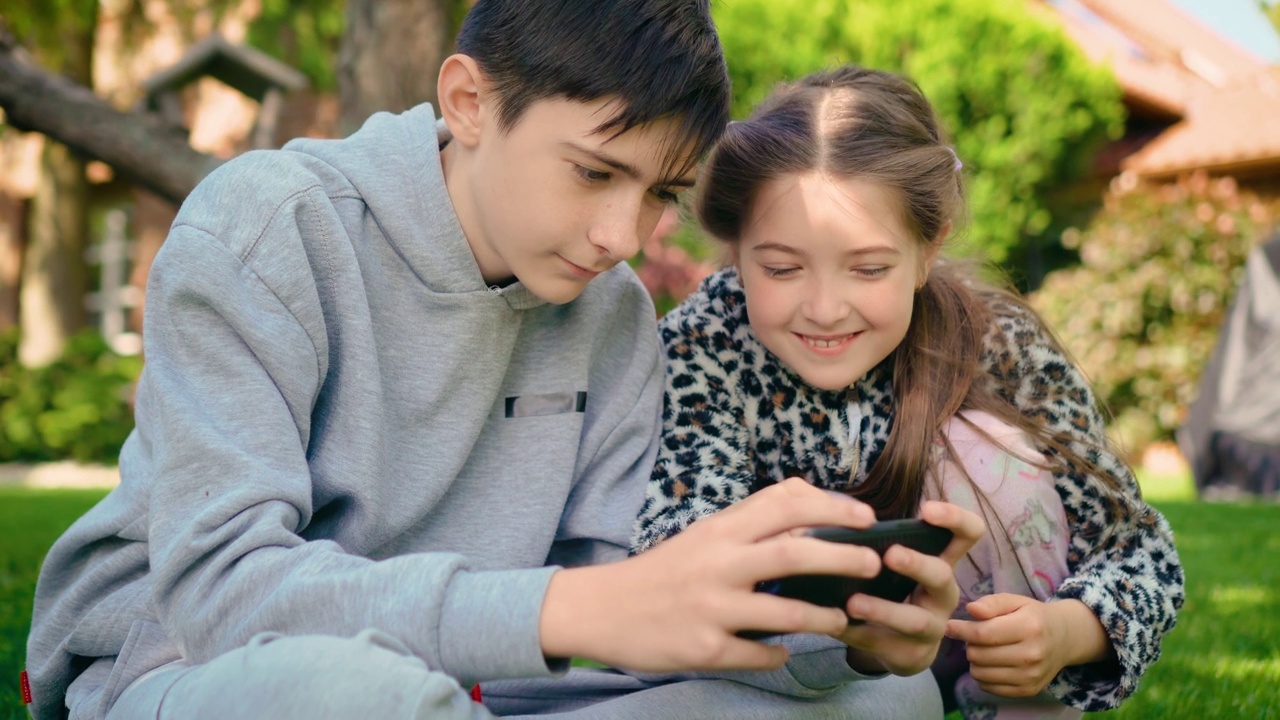 快乐的男孩和女孩在家里院子里一起玩智能手机上的手机游戏视频素材