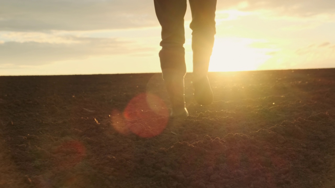 夕阳西下，农民穿着胶靴在犁过的土地上行走视频素材
