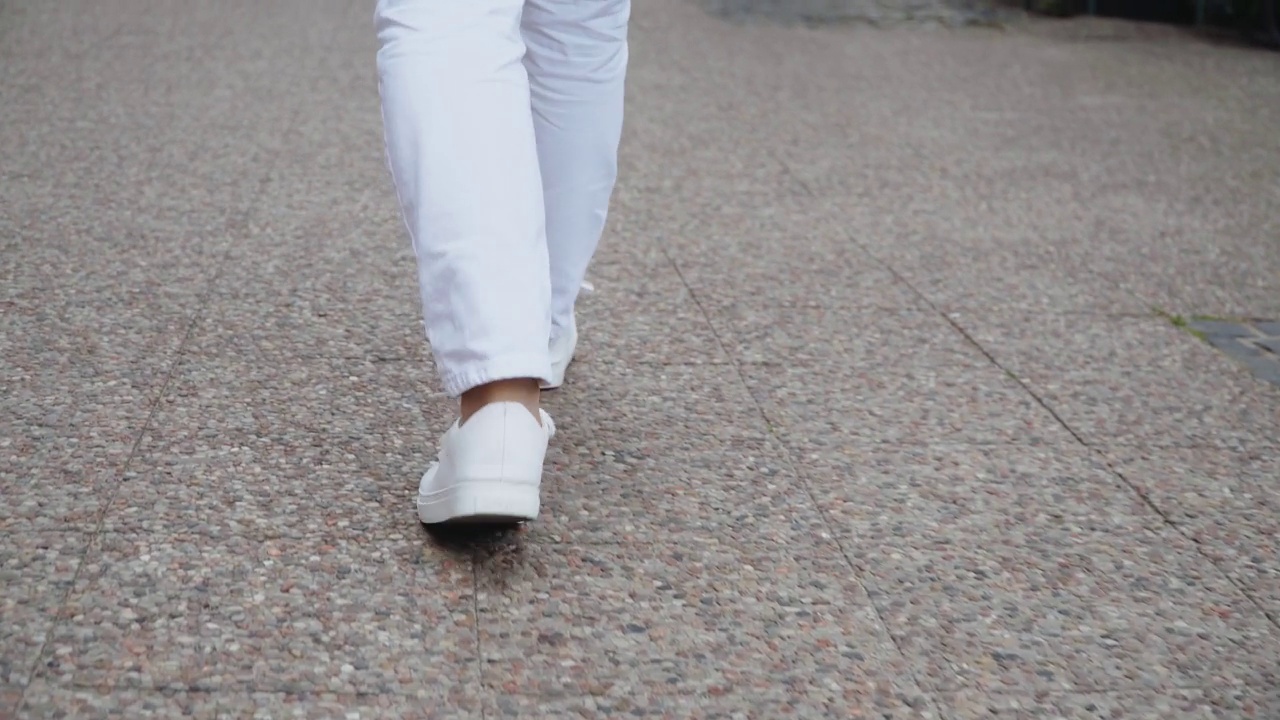 难以辨认的美丽女人的腿穿着白色的鞋子走过城市视频素材