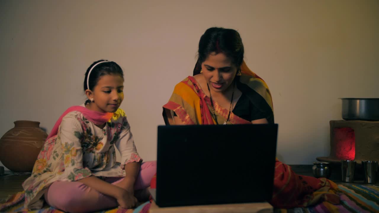年轻的母亲从她的女儿——现代村民那里学习使用笔记本电脑视频素材