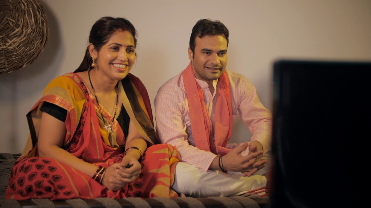 一对印度乡村夫妇坐在一张编织的小床上，开心地一起看电视视频素材