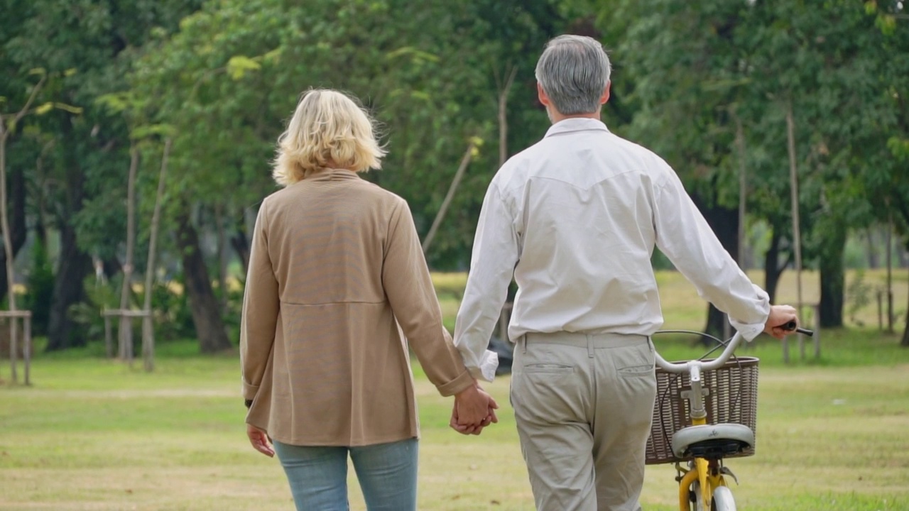 老年夫妇牵着手在公园里骑自行车散步视频素材