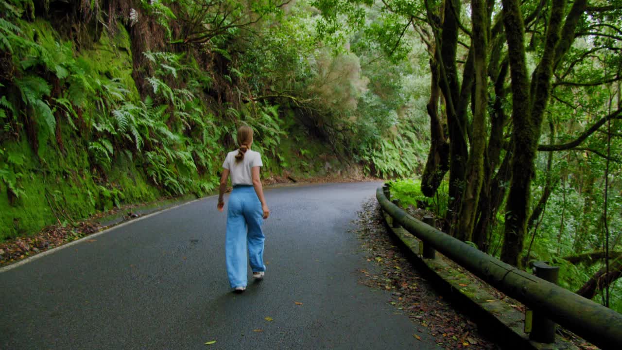一个女人走在一条柏油路在茂密的森林。在月桂树森林或丛林，阿纳加国家公园，特内里费岛，加那利群岛，西班牙。视频素材