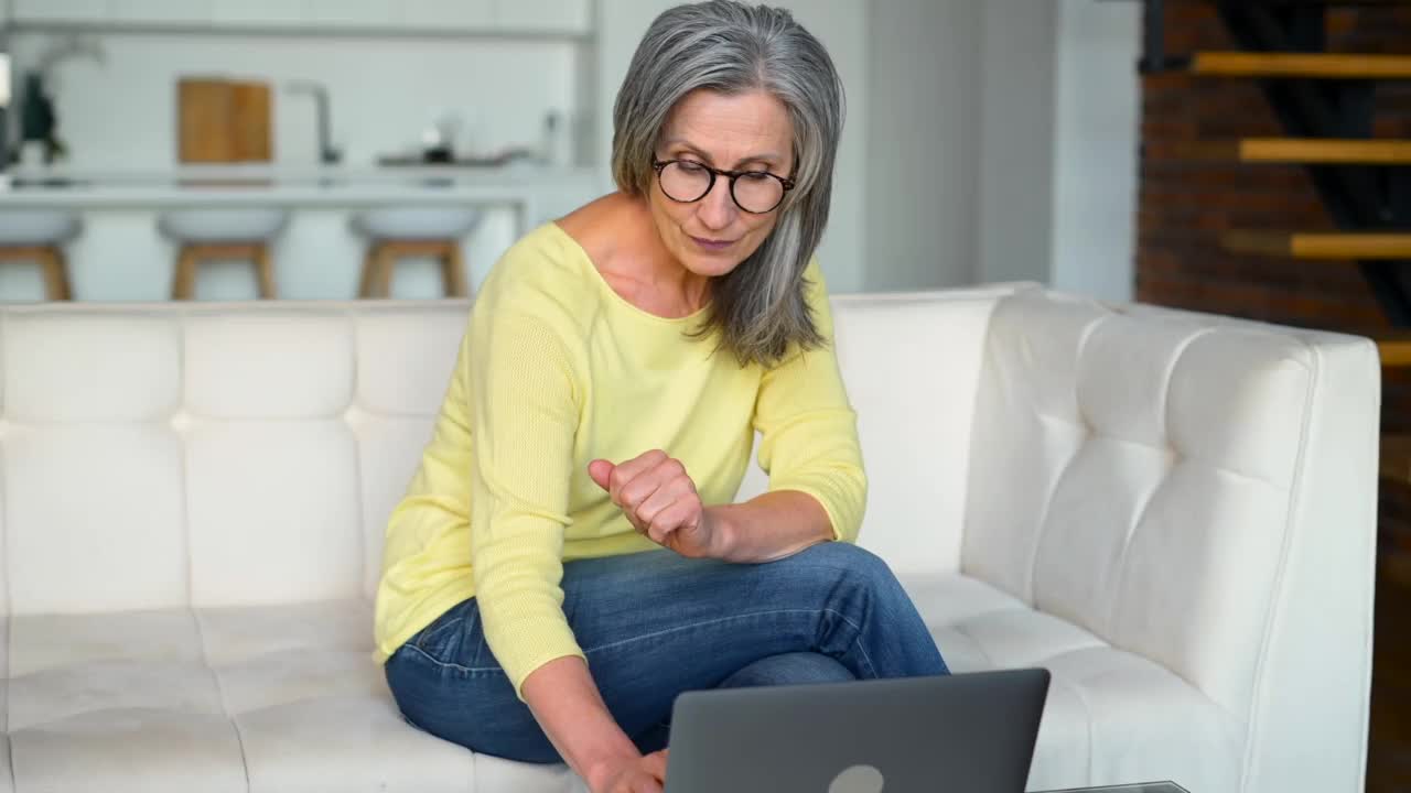 乐观的成熟中年女性在闲暇时间在家使用笔记本电脑视频素材