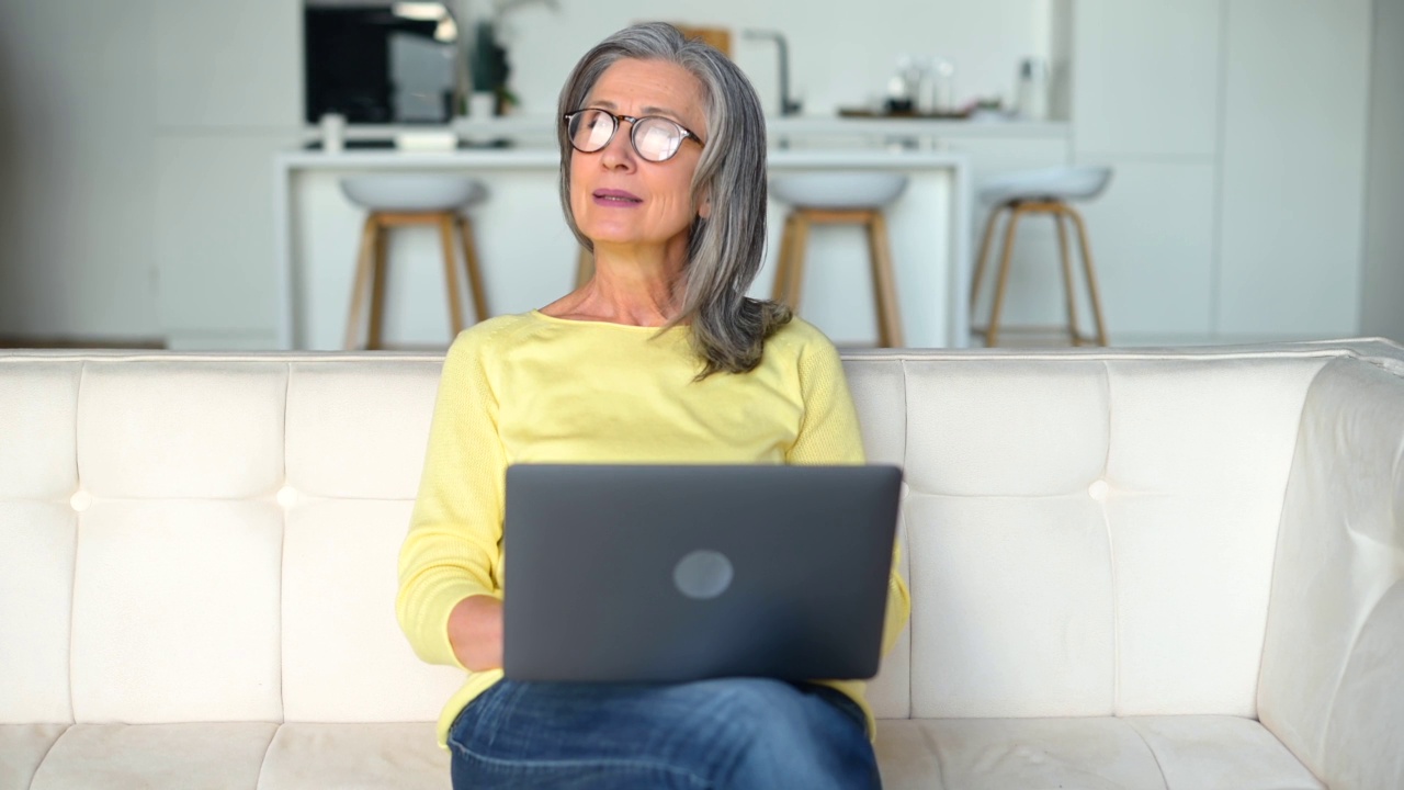 美丽积极的中年妇女坐在白色沙发上使用笔记本电脑视频素材