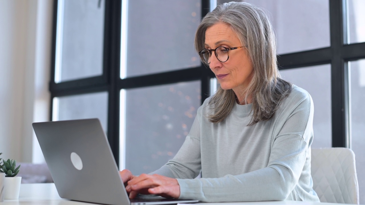 自信的商务女性在现代办公室使用笔记本电脑做文书工作，查看文件，成熟的女性企业家坐在桌子前检查报告视频素材