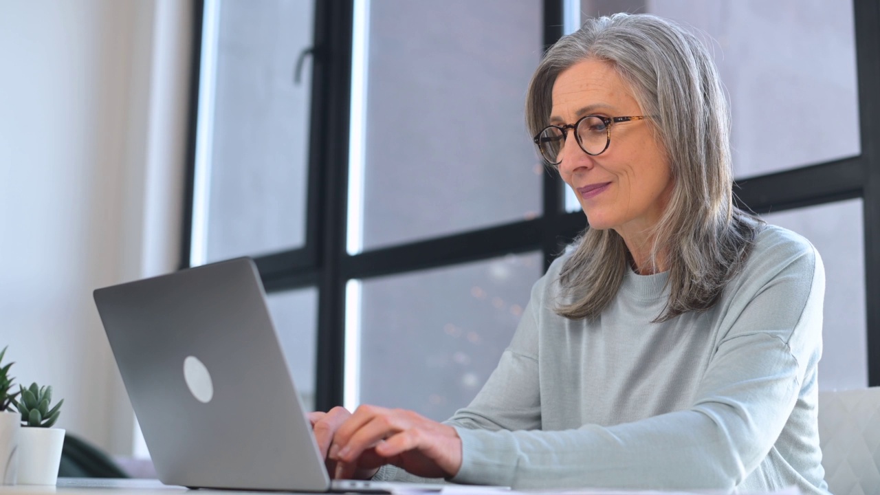时尚成熟的商务女性戴着眼镜坐在办公桌前使用笔记本电脑视频素材