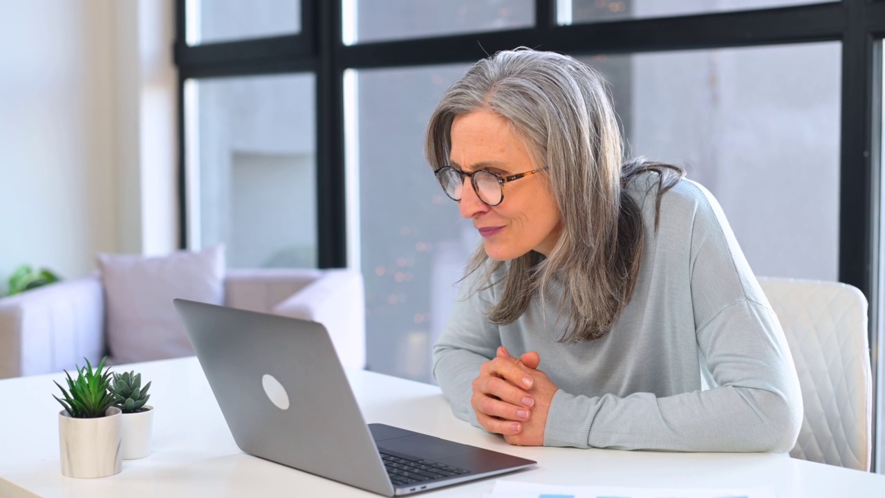 满头银发的资深女企业家开心地坐在现代化的办公室里盯着笔记本电脑屏幕，兴奋成熟的女企业家高兴地尖叫着是，收到了好消息视频素材