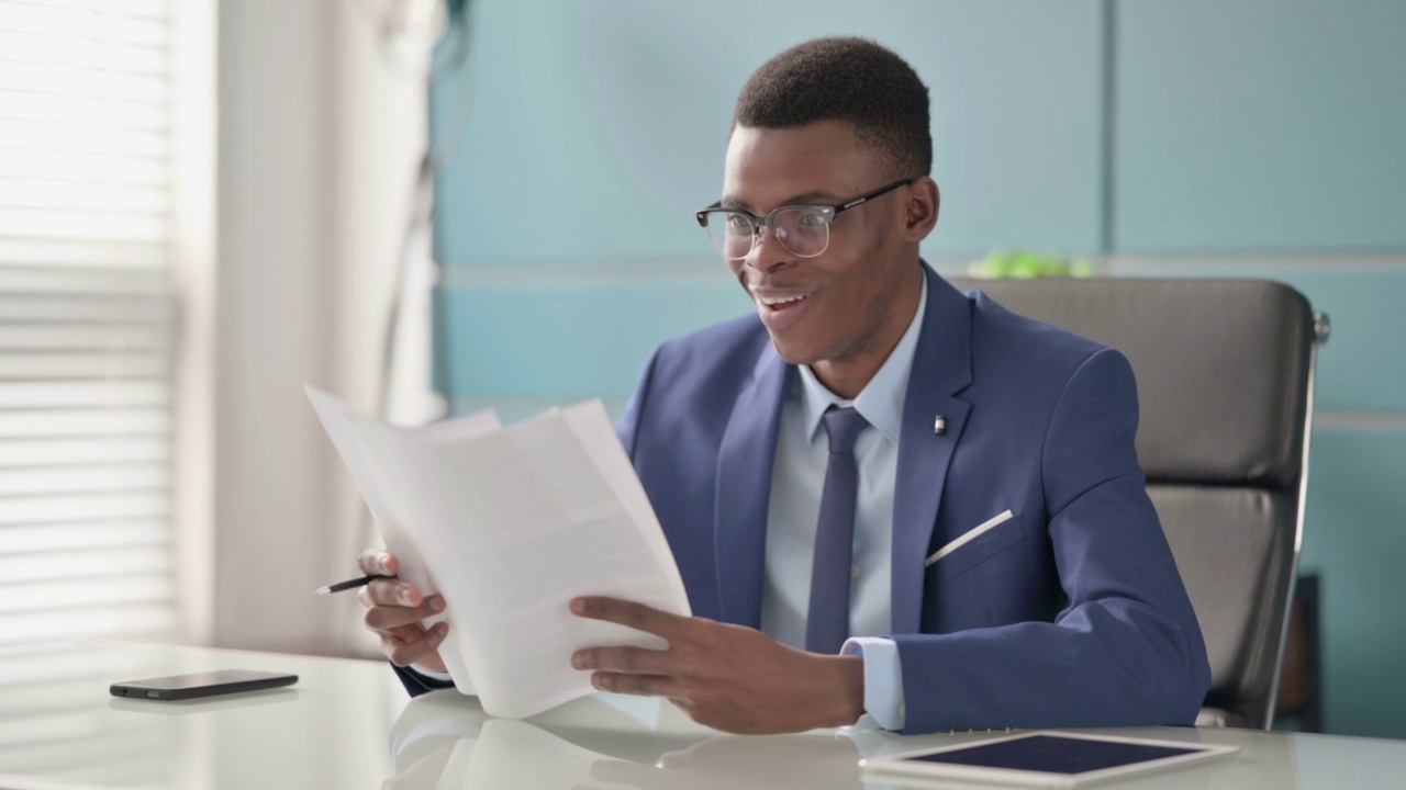 年轻的非洲商人在办公室阅读文件庆祝成功视频素材
