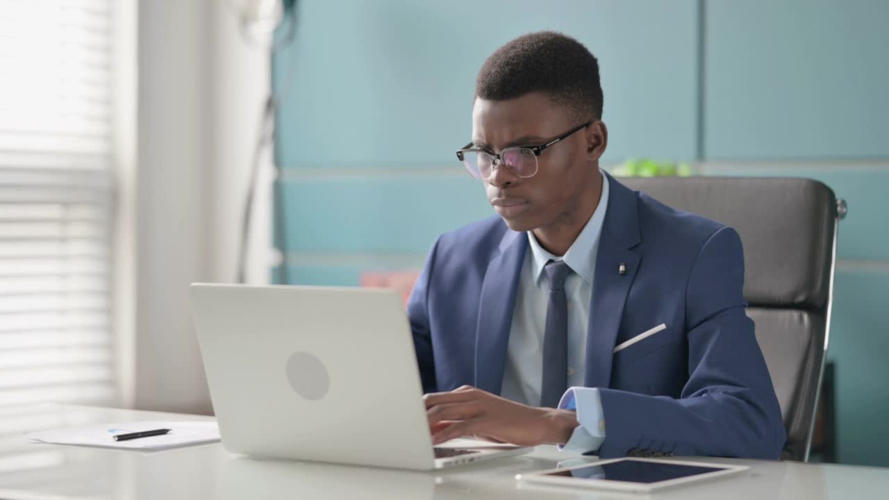 年轻的非洲商人在办公室使用笔记本电脑时背痛视频素材