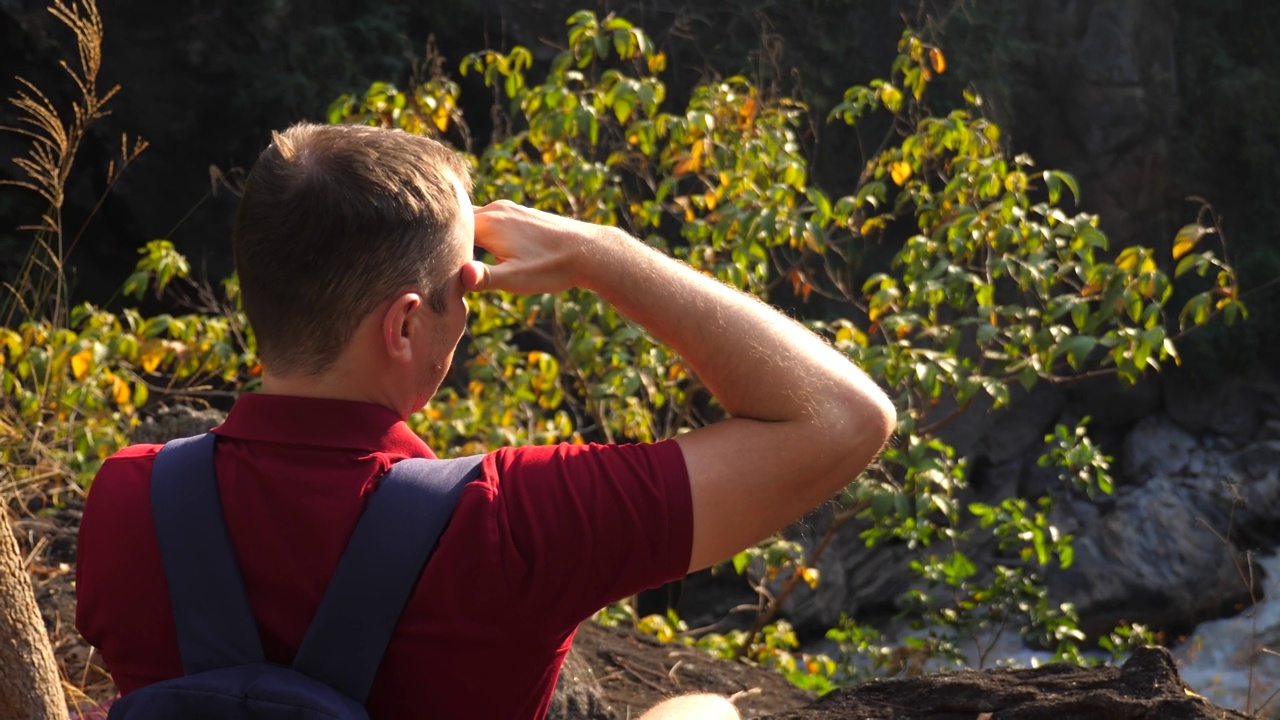背包客在峡谷边缘用手捂着额头，望着地平线。男性旅行者远眺，享受自然、日落和江景视频素材