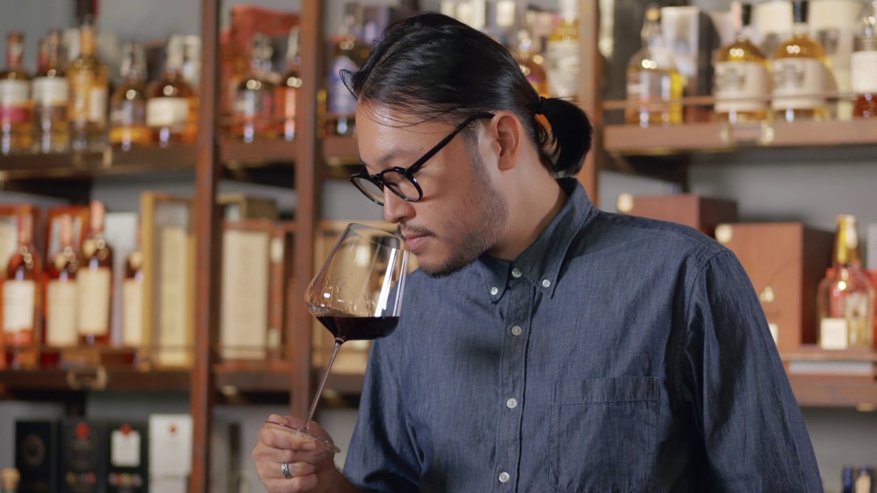 年轻的亚洲侍酒师在品尝新进口的葡萄酒时，微笑着。戴眼镜系领带的男子在酒店的餐厅酒吧品酒。视频素材