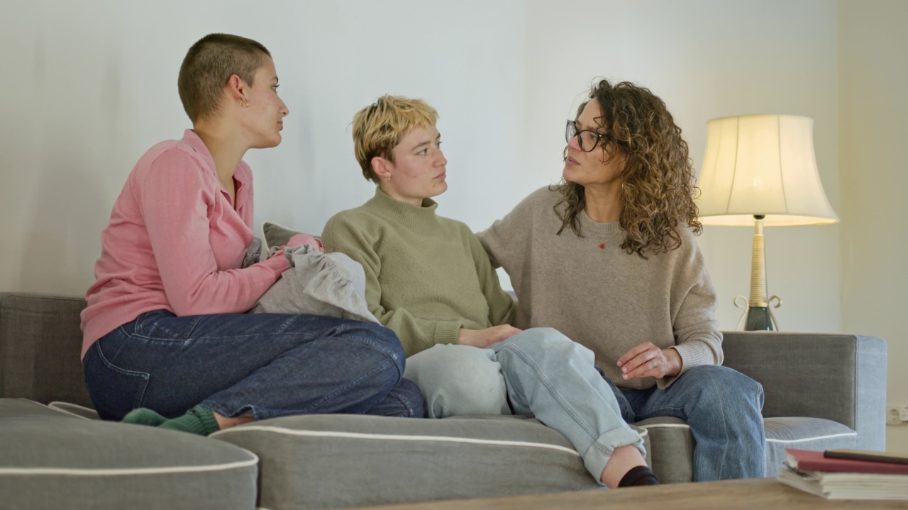 母亲和两个成年的女儿在沙发上分享失去亲人的坏消息，抚慰心灵视频素材