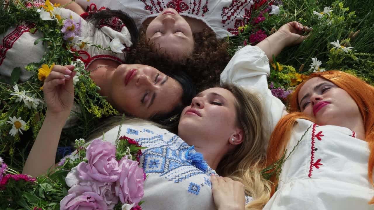 四个美丽的乌克兰女孩躺在草地上，俯瞰。乌克兰女孩们身着传统的vyshyvanka服饰，戴着花环。乌克兰民族服装。爱国主义的主题视频下载