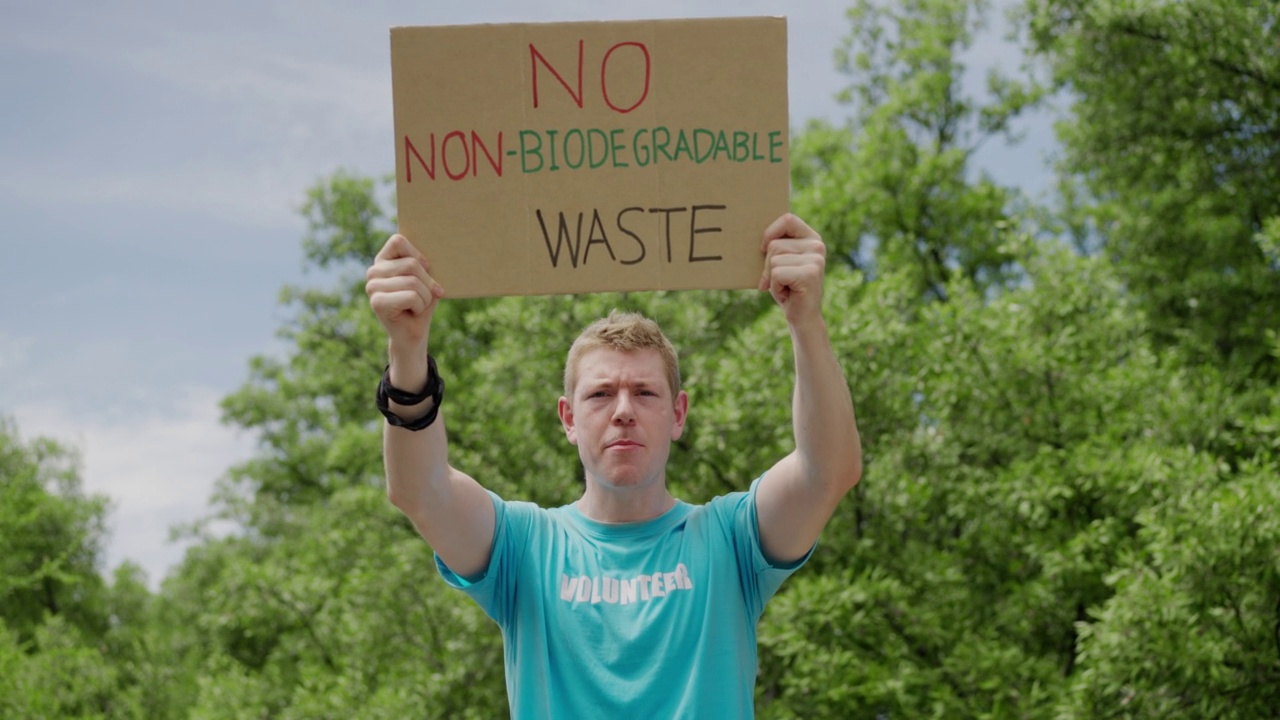 人像，正面视图:白种青年男子志愿者手持纸板认真呼吁拯救地球，不使用塑料，使用可降解塑料，拯救绿色环境，靠近森林视频下载