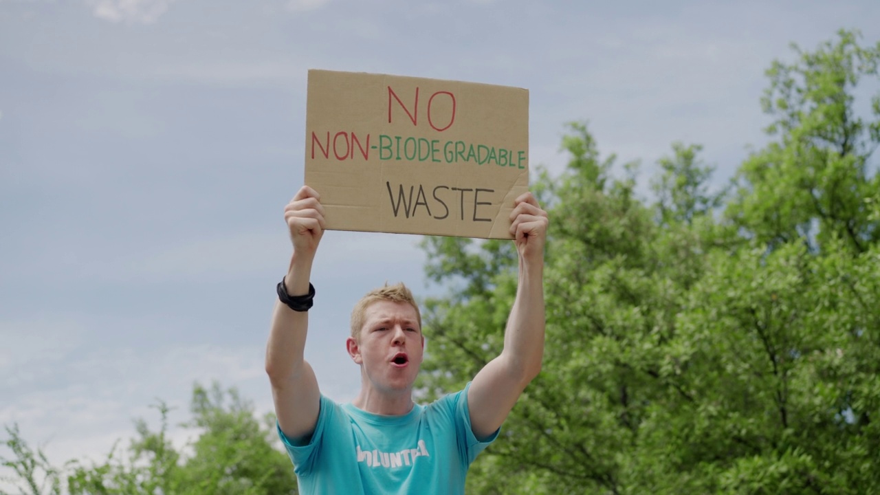 肖像:白种青年男子志愿者举着纸板认真地宣传拯救地球，不使用塑料，只使用可生物降解的塑料，拯救绿色环境，靠近森林视频下载
