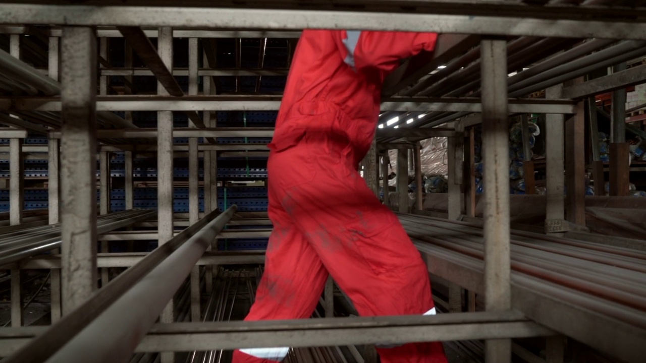 金属工业-垂直平移拍摄的亚洲工人移动的球墨铸铁管在仓库视频素材
