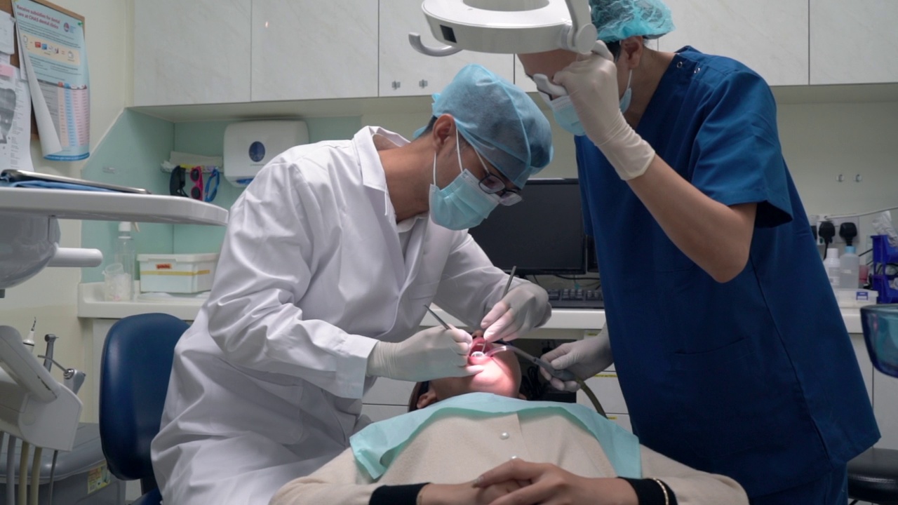 牙科护理——亚洲牙医在牙科助理在场的情况下检查他的病人时，中途更换工具视频素材