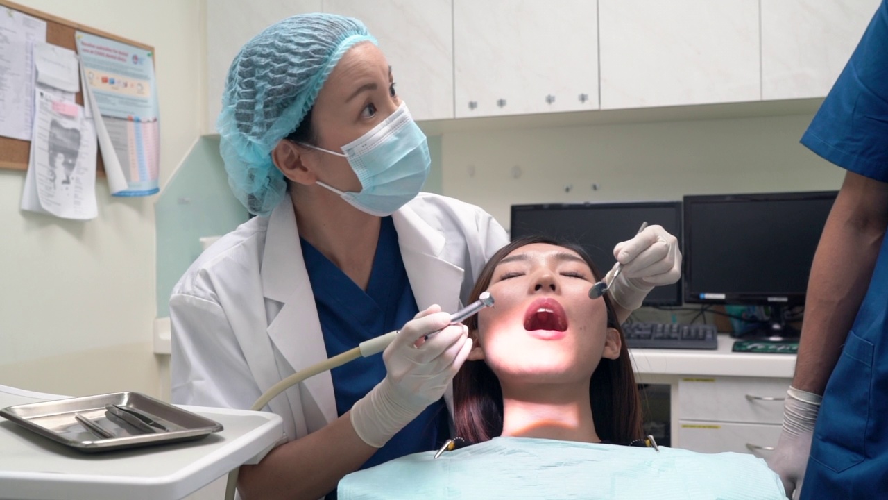 牙科保健-亚洲牙医正在进行龋齿钻孔，要求使用吸管清除唾液视频素材