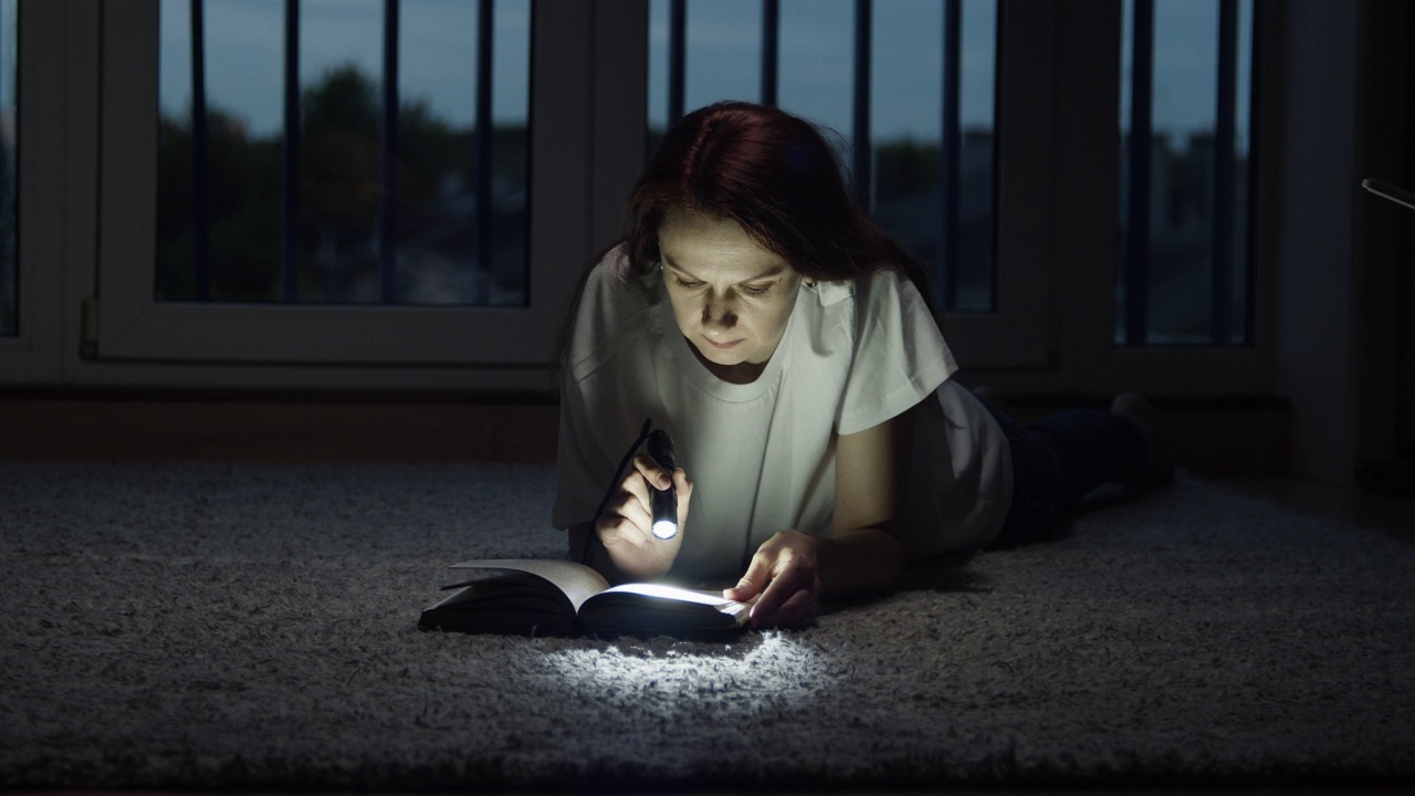 一个女人正借着手电筒的光看书。视频素材