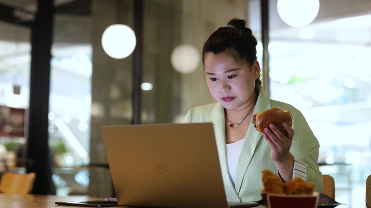 身材高大的女性在餐馆里紧张地吃汉堡包和使用笔记本电脑视频下载