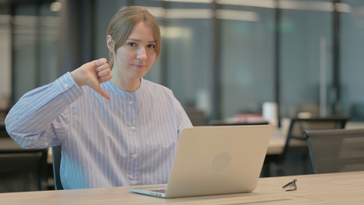 一名年轻女子在办公室使用笔记本电脑时表现出大拇指向下的手势视频素材