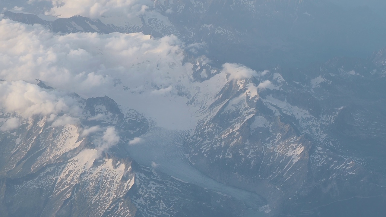 在夏季飞越欧洲的阿尔卑斯山。冰川景观。全球变暖导致的冰川融化。从飞机窗口鸟瞰视频素材