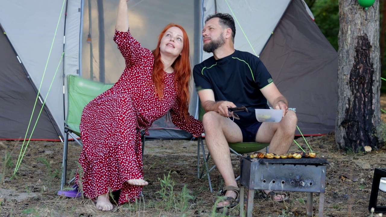 丈夫和妻子在露营，在烤架上煮肉和蔬菜，一个女人在大自然中自拍视频素材