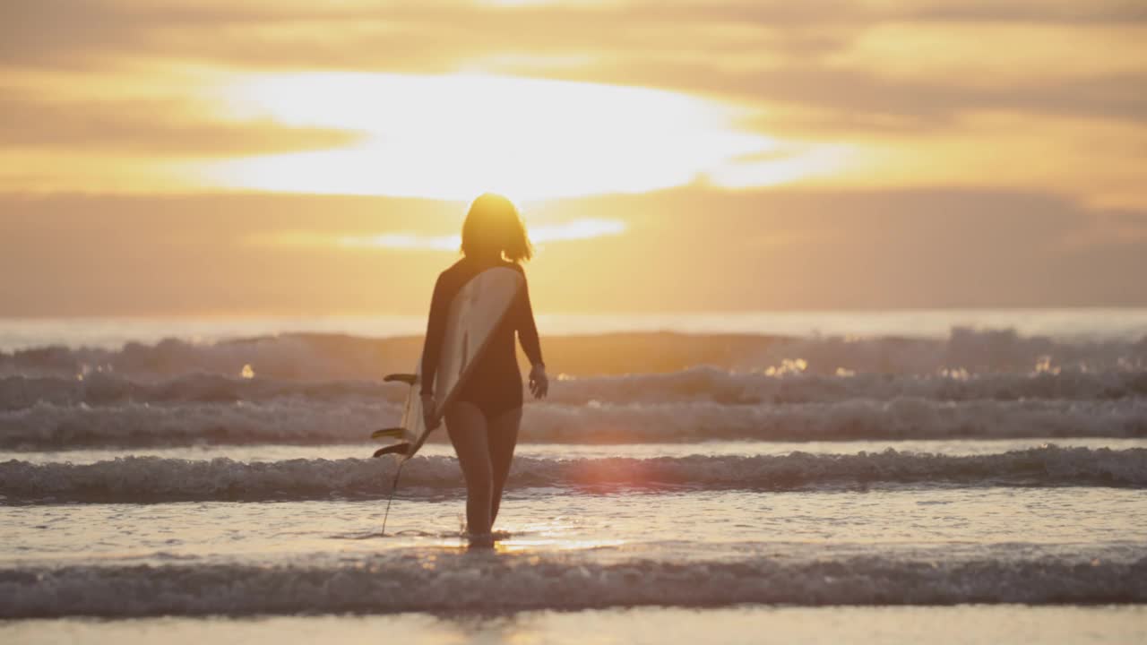 夕阳下的热带海滩上冲浪女孩的剪影。视频下载