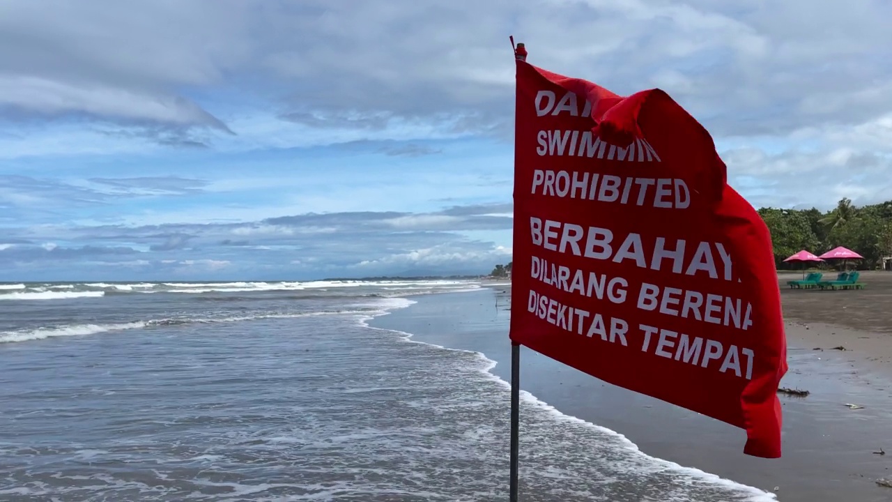 印度尼西亚巴厘岛沙滩上，危险，禁止游泳，红色警告旗和骷髅头。旗帜在狂风中飘扬，背景是暴风雨和多云的天空视频素材