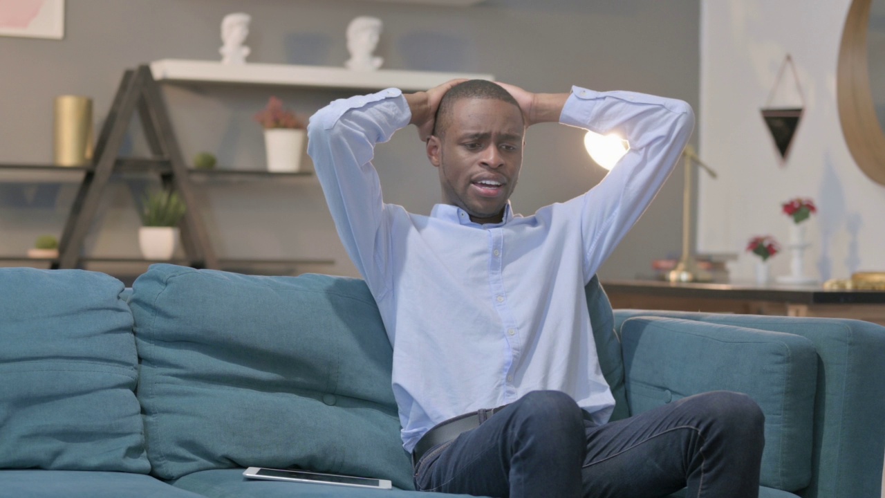 非洲男子在沙发上对平板电脑的失落反应视频素材