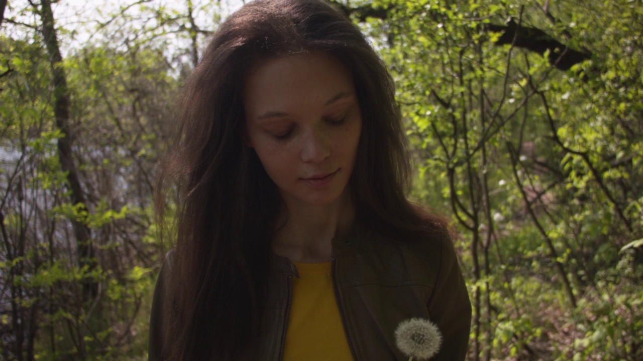 一个年轻女人在夏天的森林里吹蒲公英的特写。视频素材